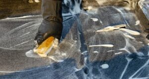 A cleaner is demonstrating carpet maintenance by scrubbing the carpet with a soapy sponge