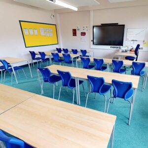 Light blue carpet installed in a school classroom with dark blue chairs and wooden desks