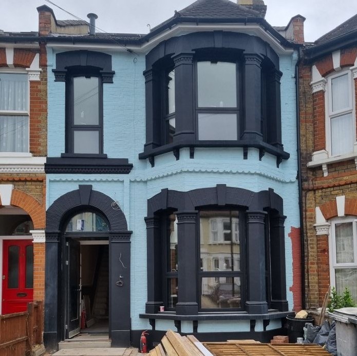 Image of the outside of the house, which is painted light blue with black paint around the doors and windows