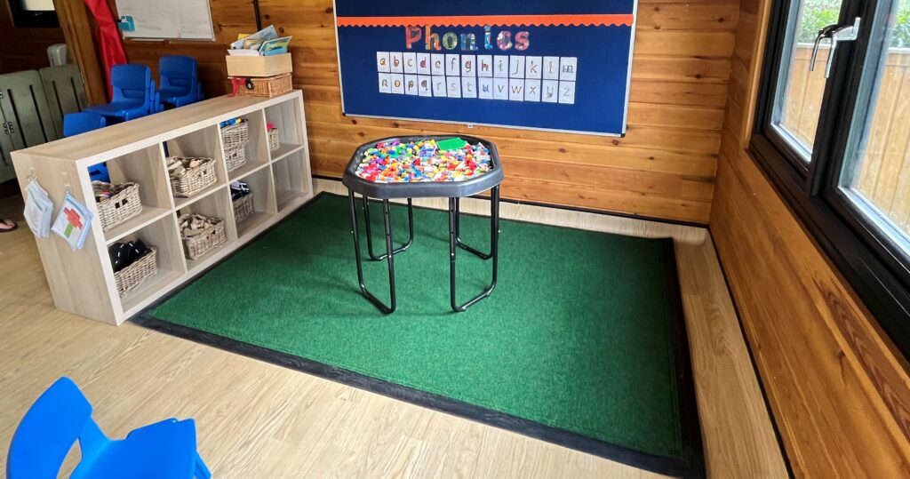 A wider view of the mat on the floor under a phonics display board inviting children to learn