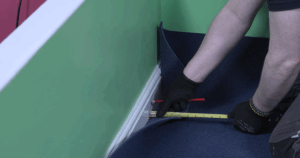 Flooring contractor measuring sheet carpet against the wall to work out how much needs cutting to fit